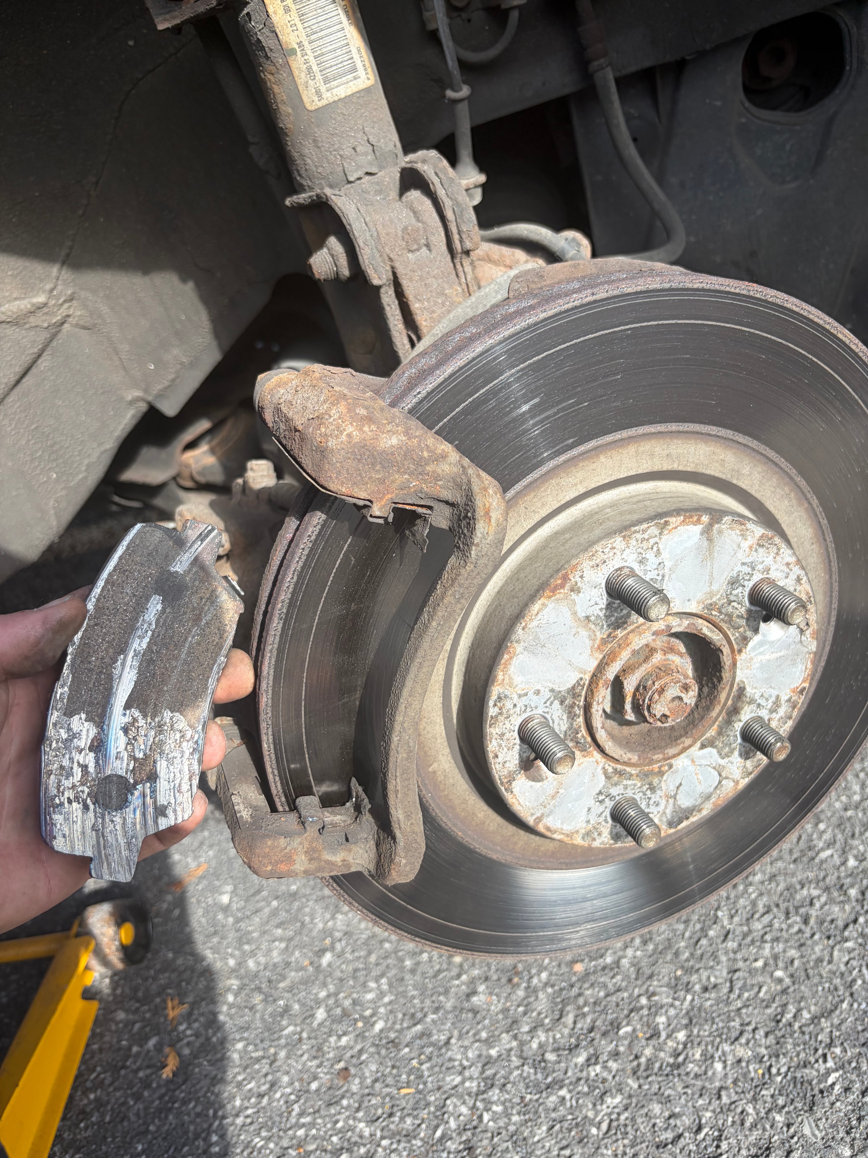 Plaquettes de frein complètement usées tenues en main devant le disque rouillé — état avant l'intervention de Caron Précision Automobile